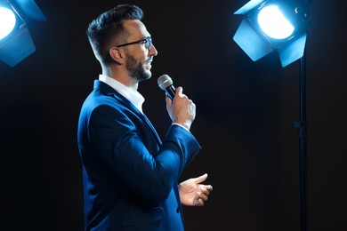 Motivational speaker with microphone performing on stage. Space for text