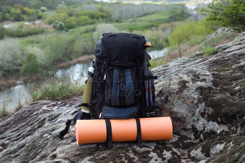 Backpack with camping mat and trekking poles on rocky hill