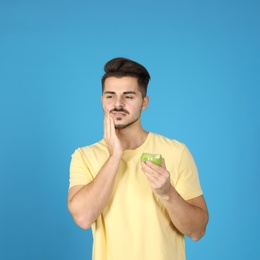 Emotional young man with sensitive teeth and apple on color background