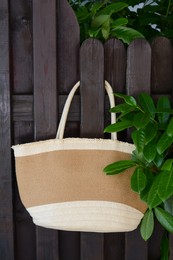 Stylish bag hanging on wooden fence outdoors. Beach accessory