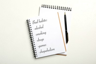 Notebook with list of bad habits on white table, flat lay