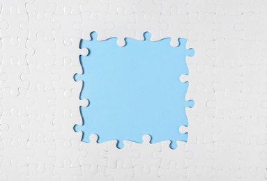 Frame made with white puzzle pieces on light blue background, top view. Space for text
