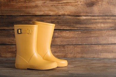 Pair of yellow rubber boots on wooden surface. Space for text