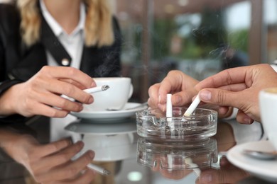 Women putting out cigarettes in ashtray at table, closeup