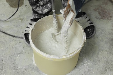 Professional worker mixing plaster in bucket indoors, closeup
