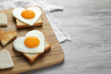 Photo of Heart shaped fried eggs with toasts on white wooden table, closeup. Space for text