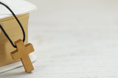 Wooden Christian cross and Bible on white table, closeup. space for text