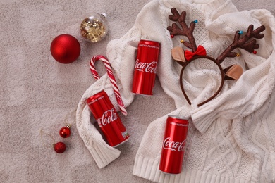 MYKOLAIV, UKRAINE - JANUARY 13, 2021: Flat lay composition with Coca-Cola cans, Christmas decor and sweater on floor