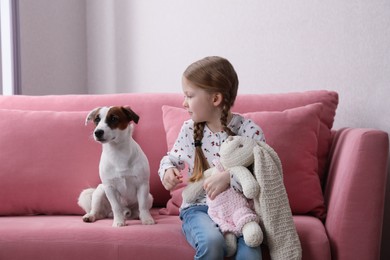 Cute little girl with her dog and toy bunny on sofa indoors. Childhood pet