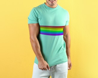 Young man wearing turquoise t-shirt with image of LGBT pride flag on yellow background