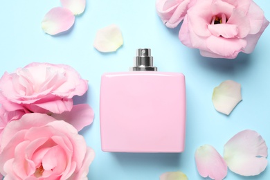 Flat lay composition with bottle of perfume and flowers on light blue background