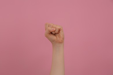 Woman raising fist on pink background, closeup