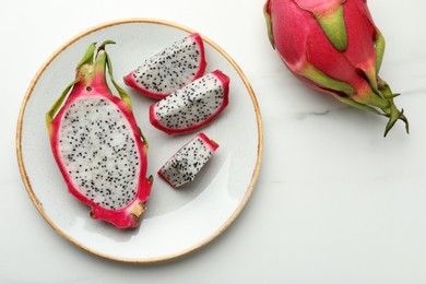 Plate with delicious cut and whole pitahaya fruits on white marble table, flat lay
