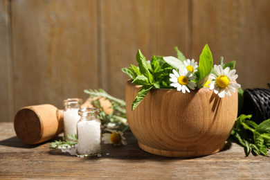 Mortar with chamomile flowers and fresh green mint on wooden table. Healing herbs