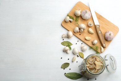 Glass jar of pickled mushrooms on white wooden table, flat lay. Space for text