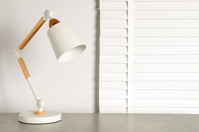 Photo of Stylish modern desk lamp on light gray table indoors, space for text