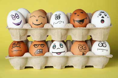 Eggs with different drawn faces in cardboard packages on pale yellow background
