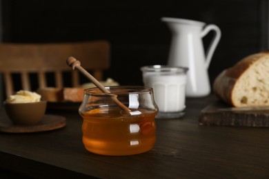 Photo of Jar with honey, milk, bread and butter on wooden table