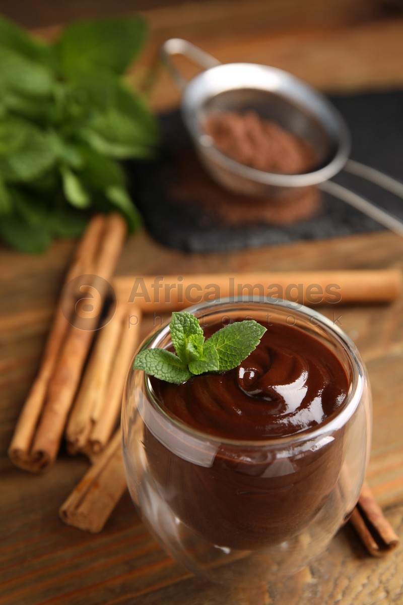 Glass of delicious hot chocolate with fresh mint and cinnamon sticks on wooden table