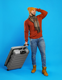 Young man in warm clothes with suitcase on blue background. Winter vacation