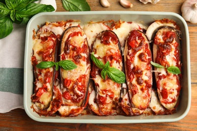 Baked eggplant with tomatoes, cheese and basil in dishware on wooden table, flat lay