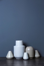 Beautiful ceramic vases on table against color wall