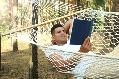 Photo of Handsome man with book relaxing in hammock outdoors on summer day