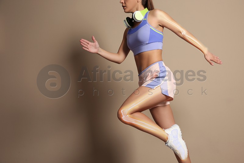 Image of Digital composite of highlighted bones and woman in sportswear with headphones running on beige background