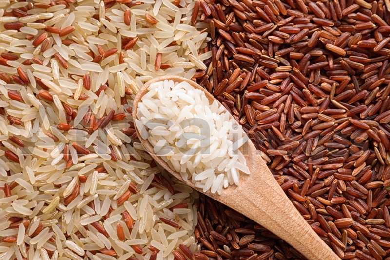 Different types of rice with wooden spoon, top view