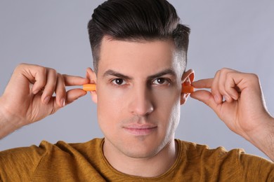 Man inserting foam ear plugs on grey background