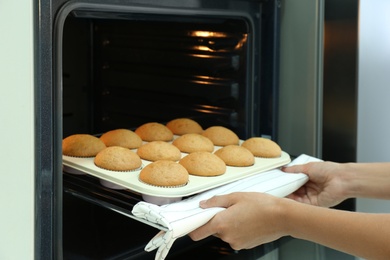 Woman taking cupcakes out of oven indoors, closeup