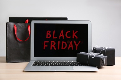 Laptop with Black Friday announcement, shopping bags and gifts on wooden table against white background