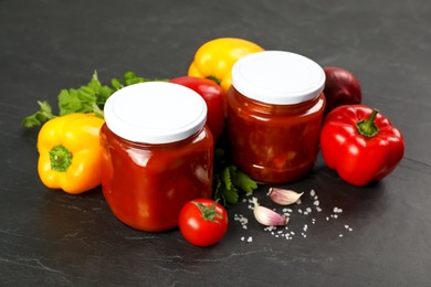 Photo of Glass jars of delicious canned lecho and fresh ingredients on black table