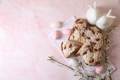 Photo of Delicious Italian Easter dove cake (traditional Colomba di Pasqua), painted eggs, figure of rabbits and branch with flowers on pink marble table, flat lay. Space for text