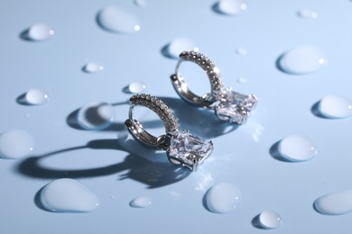 Photo of Elegant earrings on light blue surface covered with water drops. Luxury jewelry