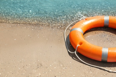 Orange life buoy on sand near sea, closeup. Emergency rescue equipment