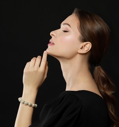 Young woman wearing elegant pearl bracelet on black background, space for text