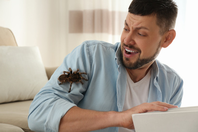 Photo of Scared man with tarantula at home. Arachnophobia (fear of spiders)
