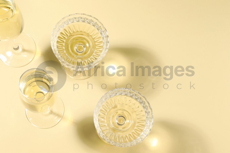 Photo of Glasses of delicious sparkling wine on light yellow background, above view. Space for text