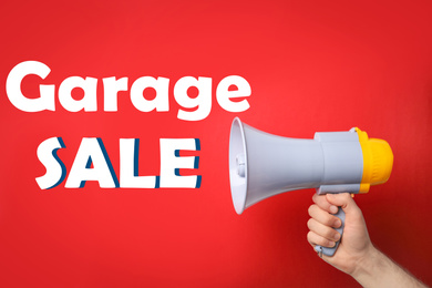 Man holding megaphone and phrase GARAGE SALE on red background, closeup