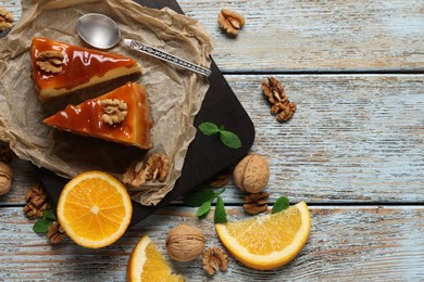 Photo of Pieces of delicious caramel cheesecake with walnuts and orange served on wooden table, flat lay. Space for text