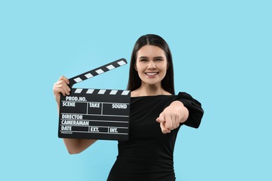 Photo of Happy actress with clapperboard on light blue background. Film industry
