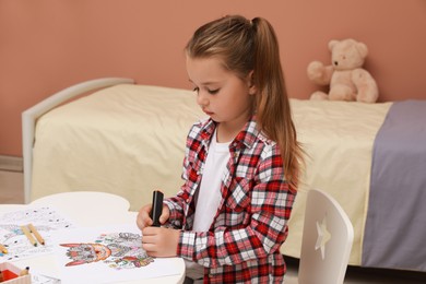 Little girl coloring antistress page at table indoors