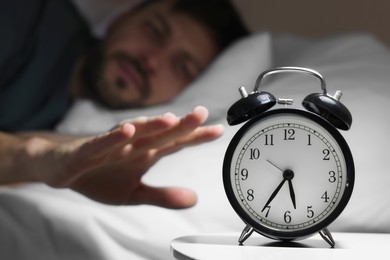 Photo of Sleepy man turning off alarm clock on nightstand in morning, closeup