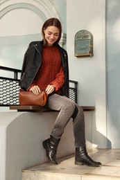 Photo of Fashionable young woman with stylish bag on bench outdoors