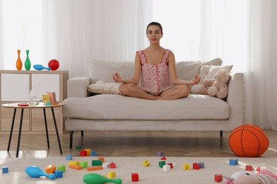 Calm young mother meditating on sofa in messy living room