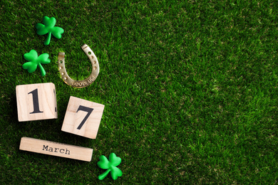 Flat lay composition with horseshoe and wooden block calendar on grass, space for text. St. Patrick's Day celebration