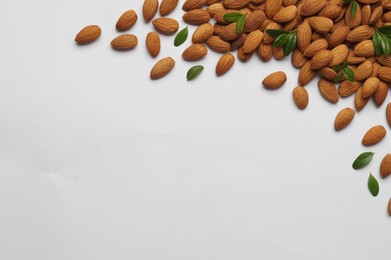 Photo of Delicious almonds and fresh leaves on white background, flat lay. Space for text