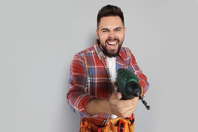 Emotional man with power drill on grey background
