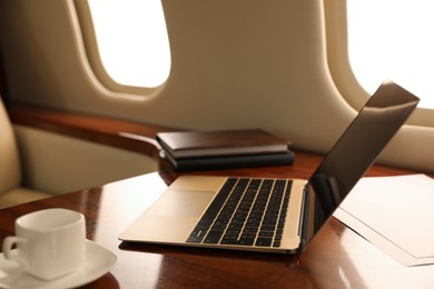 Laptop with notebooks and cup of coffee on table in airplane